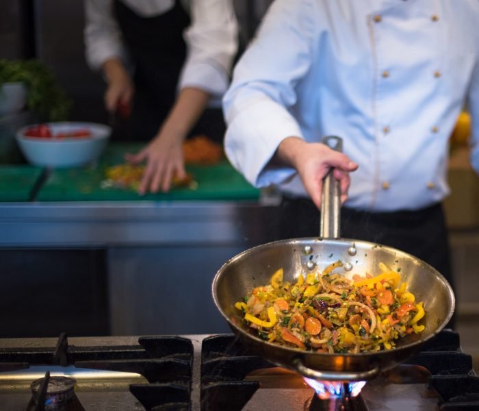 Young male chef flipping vegetables in wok at commercial kitchen