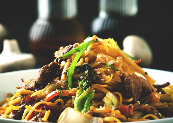 Noodles with meat and vegetables and teriyaki sauce on a dark background