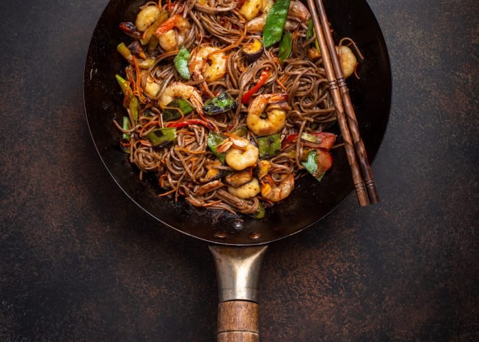 Chinese soba stir-fry noodles with shrimps, vegetables in old rustic wok pan served on concrete background, close up, top view. Traditional asian/thai dish, close up
